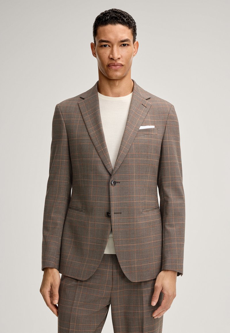 Brązowa marynarka w kratę wykonana z gładkiej tkaniny. Posiada zapięcie na dwa guziki, wyraziste klapy oraz kieszeń na piersi z białą chusteczką.