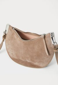 Borsa a spalla in suede color testa di moro con forma arrotondata a mezzaluna. Caratterizzata da una chiusura a zip in argento e un interno liscio. Include una tracolla regolabile.