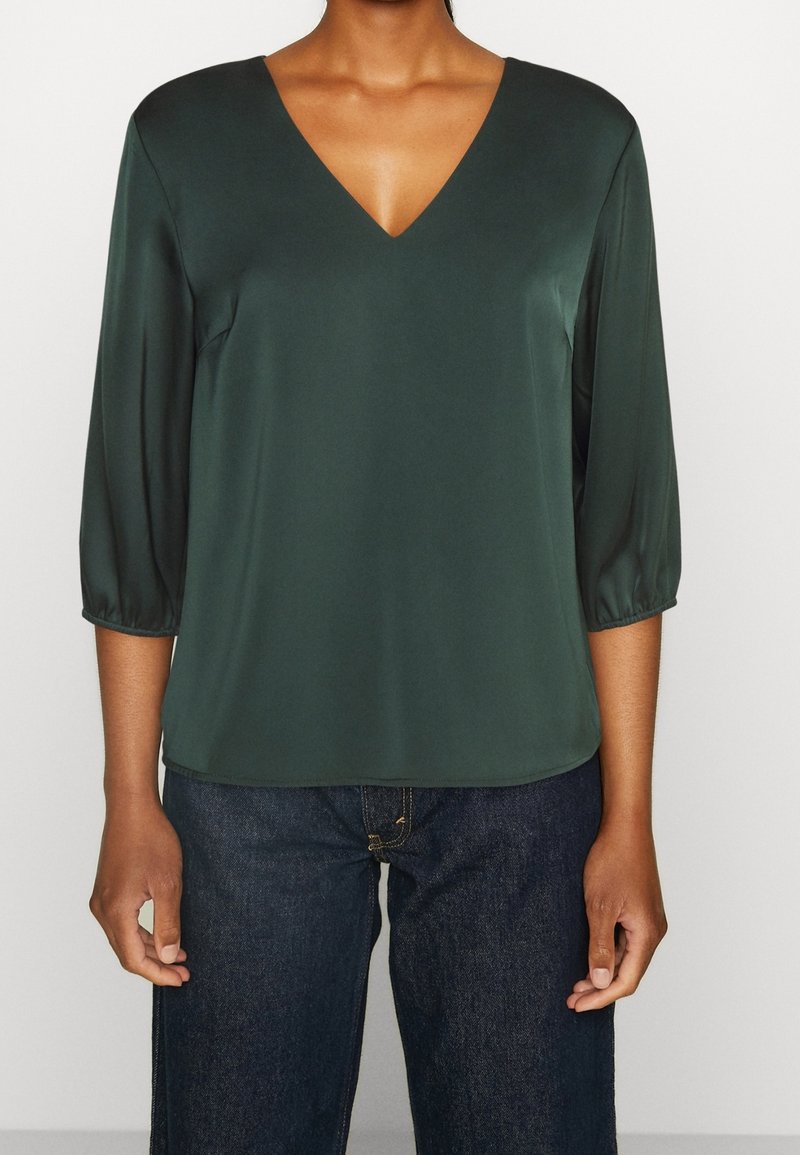 Dunkelgrüne Satin-Bluse mit V-Ausschnitt, dreiviertel Ärmeln und lässiger Passform. Glatte Textur mit minimalen Nähdetails.