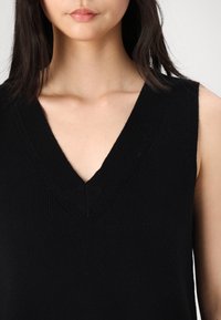 Maglione senza maniche nero a scollo a v con texture a costine e un profondo scollo appuntito, che mette in risalto linee pulite e una silhouette aderente.