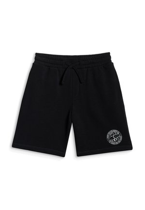 Młody chłopiec ubrany w czarną bluzę z kapturem i zamkiem, biały t-shirt z nadrukiem, czarne spodenki, czarno-białe trampki, białe skarpetki oraz czarną wzorzystą chustę na szyję.