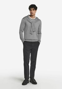 Grå tröja med en ögla design runt halsen, i kombination med mörka byxor och svarta skor, vilket visar en enkel, avslappnad stil.