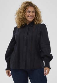 Camisa negra de botones con rayas texturizadas y detalles de encaje, que presenta mangas abullonadas y puños fruncidos. Tela suave con un ajuste entallado.