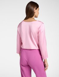 Rosa Satinbluse mit Dreiviertelärmeln; glatte Textur und weiter Ausschnitt. Kombiniert mit rosa maßgeschneiderten Hosen.