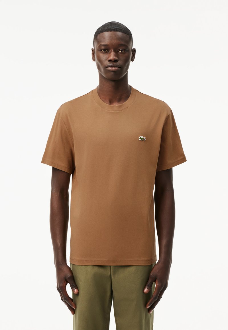 T-shirt in cotone marrone con scollo rotondo, maniche corte e un piccolo logo Lacoste verde e bianco sul lato sinistro del petto.