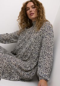 Robe à motifs floraux en crème et marine, à manches longues avec un col haut, en tissu doux, avec des détails froncés à la taille.