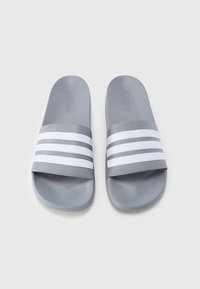 Γκρι σαγιονάρες με λευκές τριπλές ρίγες στα λουράκια, κατασκευασμένες από λείο συνθετικό υλικό. Επίπεδη σόλα και ανοιχτή μύτη.