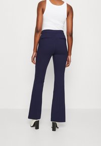 Pantalon évasé bleu marine avec une taille haute, confectionné dans un tissu lisse, doté de deux poches arrière et d'une silhouette épurée.