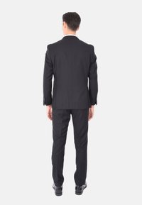 Abito nero con una vestibilità su misura, spacco singolo sul retro e pantaloni abbinati. Tessuto liscio con una lucentezza sottile, abbinato a scarpe eleganti nere.