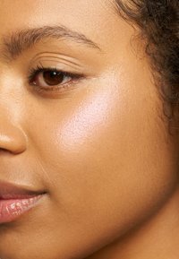 Gros plan sur une texture de peau avec une finition brillante, présentant des tons marron clair, des poils fins le long de la mâchoire et une apparence naturelle et hydratée.