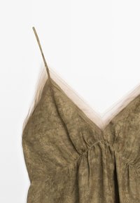 Olive green dress with thin straps, a V-neckline, and sheer overlay. Soft texture with gathered detailing at the bust.