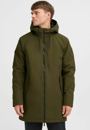 Parka impermeable verde oliva con capucha, que cuenta con una cremallera frontal, bolsillos laterales y un logo bordado en la manga izquierda.