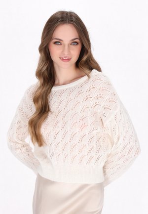 Pull en tricot blanc au fit ample, avec un motif en vague, des manches larges et un ourlet côtelé. Porté sur une jupe en satin beige.