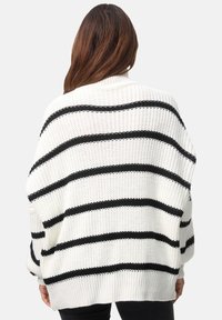 Weißer Strickpullover mit schwarzen horizontalen Streifen, lockerer Schnitt, weite Ärmel und gerippter Saum. Die Textur wirkt weich und robust.