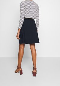 Randig långärmad topp i kombination med en mörk A-linjeformad kjol och burgundy klacksandaler med remmar, vilket visar en ren och avslappnad silhuett.