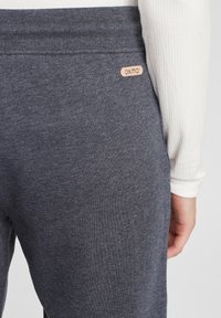 Grå joggingbyxor i mjukt material med en ribbad midjeband och en liten beige lapp med varumärket "oxmo" på baksidan.