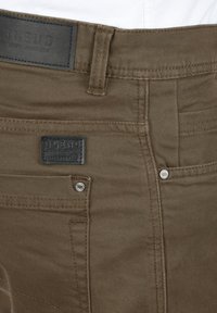 Pantalones de mezcla de algodón marrones con una tela texturizada, herrajes plateados y una etiqueta de cuero negro con "BLEND" grabada en ella.