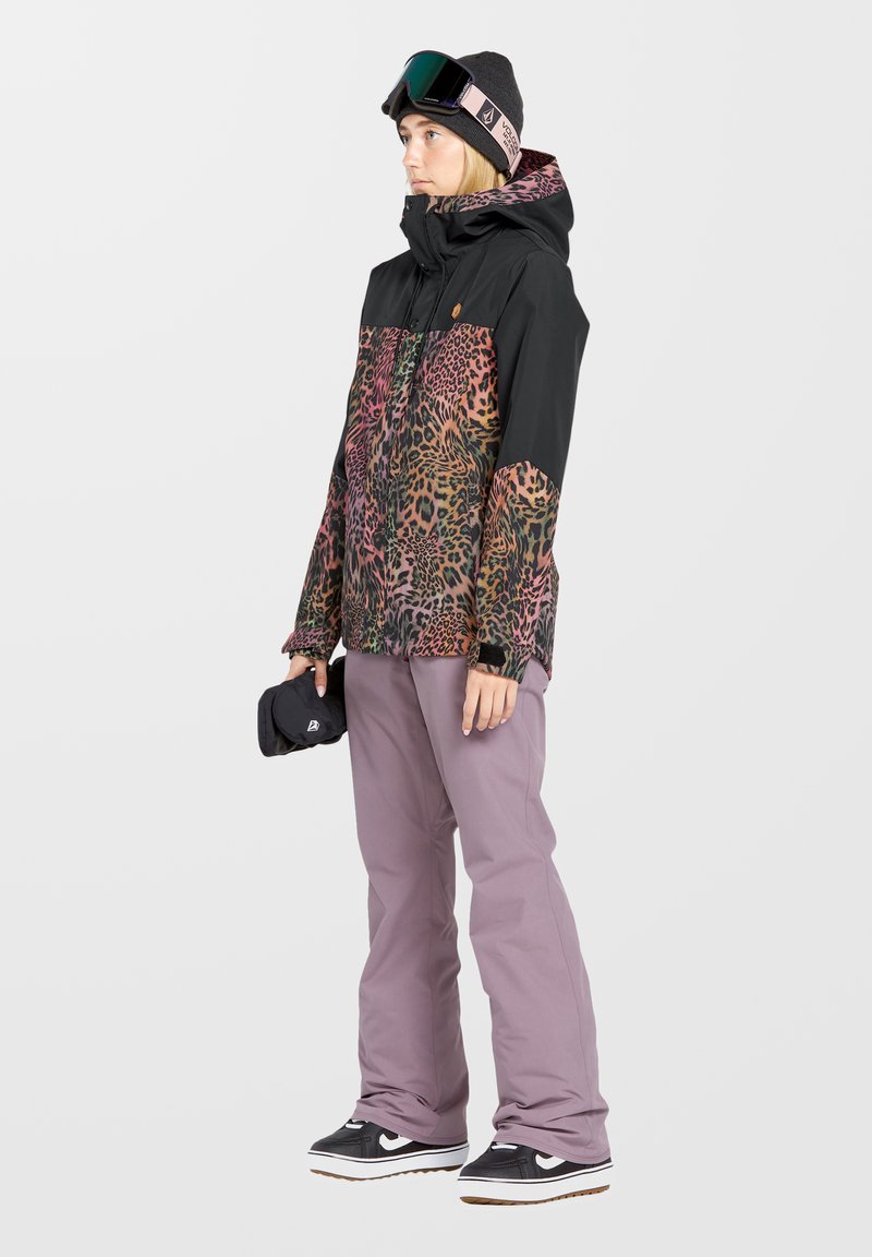 Färgglad leopardmönstrad snöjacka med svart överdel och rosa detaljer, kombinerad med ljuslila snöbyxor och svarta sneakers.