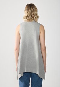 Sleeveless gray top made of soft fabric, featuring a longer back hem and a relaxed fit, paired with blue jeans.