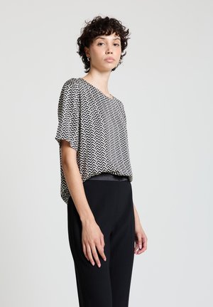 Top a maniche corte con motivo a zigzag in bianco e nero, vestibilità ampia, scollo arrotondato, abbinato a pantaloni neri a vita alta. Tessuto dalla texture liscia.