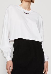 Weißes, kurz geschnittenes Langarmshirt aus Baumwolle mit lockeren Ärmel. Kombiniert mit einem schwarzen Ripprock. Einfaches Design ohne Muster.