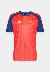 Εθνική φανέλα ποδοσφαίρου της Ισπανίας, κόκκινη με μπλε λεπτομέρειες, με κάθετες ρίγες, κίτρινο λογότυπο και λεπτομέρειες στους ώμους.