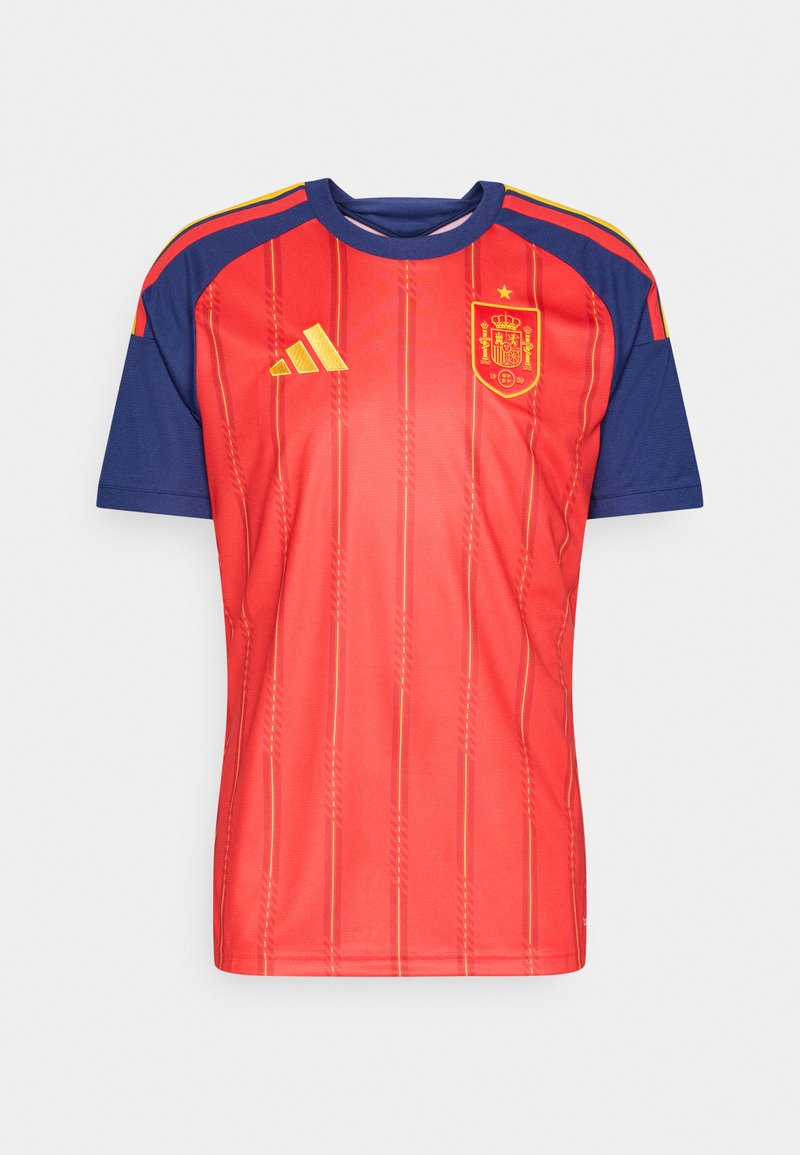 Εθνική φανέλα ποδοσφαίρου της Ισπανίας, κόκκινη με μπλε λεπτομέρειες, με κάθετες ρίγες, κίτρινο λογότυπο και λεπτομέρειες στους ώμους.