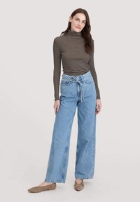 Gestreifter Rollkragenpullover in Schwarz und Braun, kombiniert mit hochgeschnittenen, weit geschnittenen hellblauen Jeans. Auffällige Gürtelschlaufen und vordere Taschen.