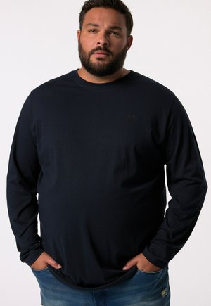 Navy longsleeve T-shirt van zacht stof, met een ronde halslijn en een klein donker logo op de linkerkant van de borst. Gecombineerd met versleten denim.