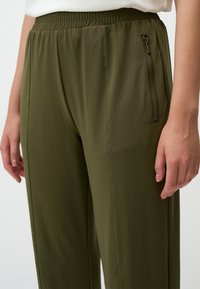 Olijfgroene lichtgewicht broek met een ontspannen pasvorm, voorzien van een elastische tailleband en een ritszak aan de zijkant voor extra functionaliteit.