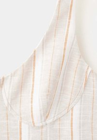 Gros plan d’un tissu blanc avec des rayures verticales beiges et orange clair et des détails de couture visibles.