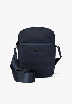 Navy blue crossbody bag made of textured nylon, featuring a front zip pocket and adjustable strap. Accent with logo detail on front.