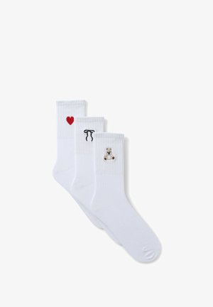 Tre paia di calze bianche con design ricamati: un cuore rosso, un nastro nero e un orsetto marrone. Tessuto misto cotone, polsini a coste.