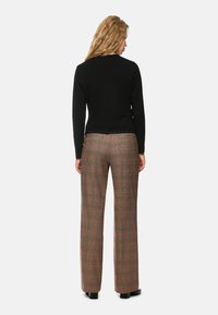 Schwarzes Langarmoberteil kombiniert mit Karohosen in Braun-, Rot- und Grüntönen sowie weitem Bein.