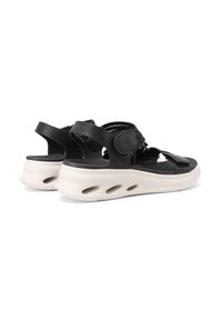 Sandali neri con un mix di materiale liscio e testurizzato, cinturini in Velcro e una suola bianca spessa con ritagli per la traspirabilità.