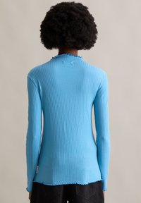 Blaues, geripptes Langarmoberteil mit einem gewellten Ausschnitt und Saum. Hergestellt aus einem dehnbaren Strickmaterial und hat eine enganliegende Silhouette.