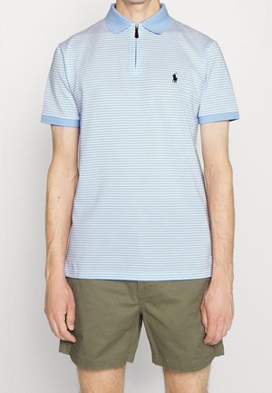 Mies, joka pukeutunut vaaleansininen ja valkoinen raidallinen lyhythihainen poolopaita, jossa pieni tumma logo, yhdistetty oliivinvihreisiin polvipituisiiin shortseihin.