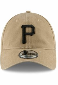 Gorra de béisbol beige con un logo bordado en negro de la letra "P". Presenta un visera curva y una correa ajustable. Tejido suave y texturizado. Etiqueta New Era 9TWENTY.