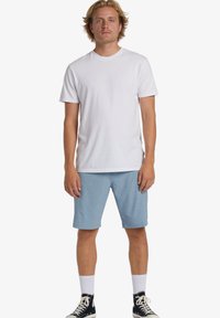 White cotton t-shirt with short sleeves, paired with light blue shorts and black high-top sneakers, featuring white ankle socks.