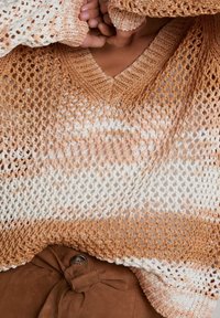 Pull en maille avec un col en V, un tissage lâche et un dégradé de tons beige clair à foncé, associé à un pantalon marron taille haute.
