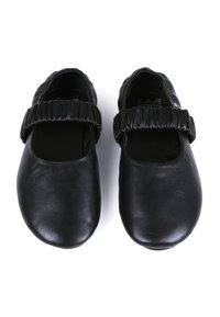 Zapatos de cuero negros con punta redonda y una correa elástica recogida en la parte superior. Textura suave con un diseño minimalista.