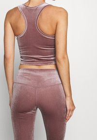 Top corto senza maniche in velluto di un morbido color malva, abbinato a leggings high-waisted coordinati; texture liscia e design aderente.
