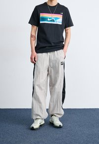 Černé tričko s barevným logem Nike, kombinované s lehkými šedými tepláky s černými bočními panely a malou nášivkou s logem.