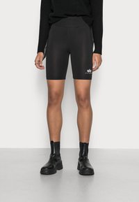 Sorte cykelshorts med høj talje, glat tekstur, der når midt på låret, med detalje af hvidt logo på underbenet. Matchet med sorte ankelstøvler.