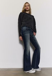 Sivi džemper, tamnoplave traperice trapezastog kroja s izblijedjelim detaljima i srebrnima tenisicama. Traperice imaju klasičan dizajn s pet džepova i bijelim šavovima.