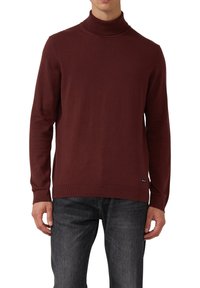 Bordowy sweter z golfem wykonany z miękkiej dzianiny, o dopasowanym kroju, z prążkowanym dekoltem i długimi rękawami. W zestawie z ciemnymi dżinsami.