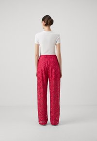 Pantaloni in pizzo di un vivace rosa, caratterizzati da una vestibilità comoda, gambe larghe e intricati motivi floreali, con un alto punto vita, abbinati a una maglia bianca.