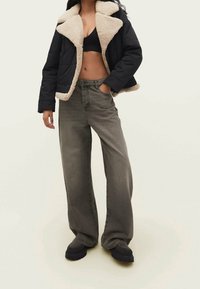 Svart pufferjacka med beige falsk fårskinnskrage, tillsammans med vida grå jeans och svarta platåstövlar. Släta tygtexturer är synliga.
