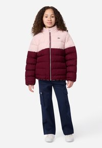 Bordo ir rožinės spalvos pūkinė striukė su aukštu kraštu, užtrauktuku ir logo detale. Sukomplektuota su tamsiai mėlynomis kargo kelnėmis ir baltomis sportinėmis bateliais.