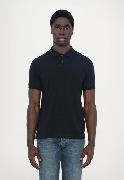 Camiseta polo navy con cuello, tres botones, mangas cortas y un diseño ajustado. Llevada con jeans de mezclilla azul claro.